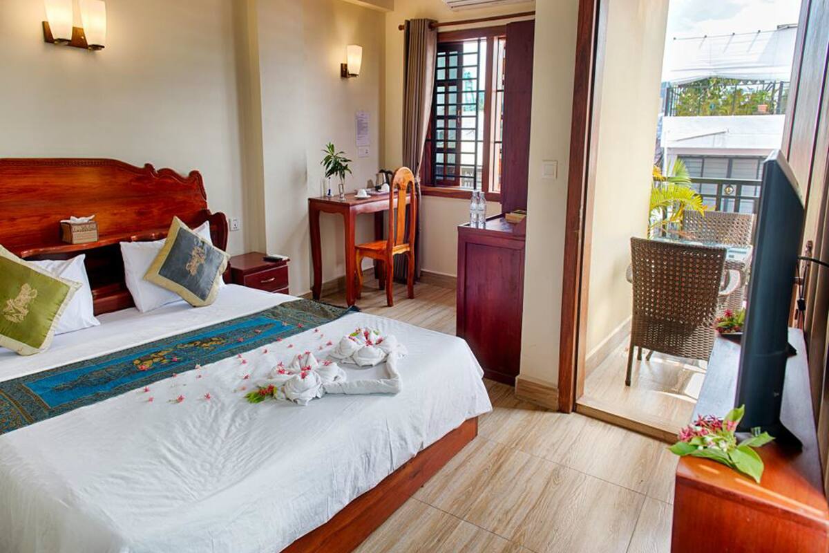 Een hotelkamer met een groot bed, een bureau, een stoel en een balkon met rieten meubels.