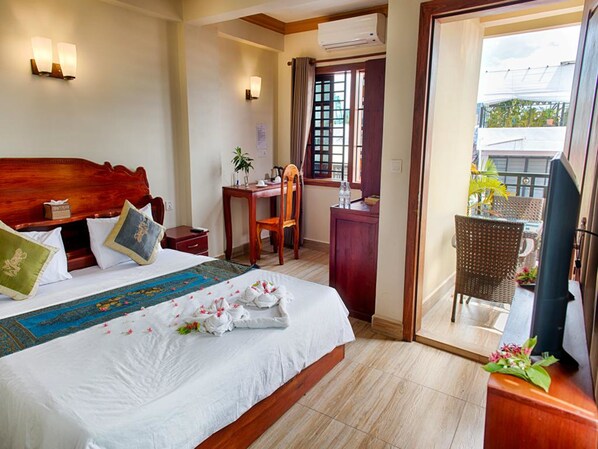 A hotel room with a large bed, a desk, a chair, and a balcony with wicker furniture. - Dynsey Boutique Hotel (Phnom Penh)