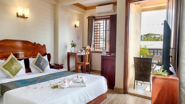 A hotel room with a wooden bed, a desk, a chair, and a balcony with a view. - Dynsey Boutique Hotel (Phnom Penh)