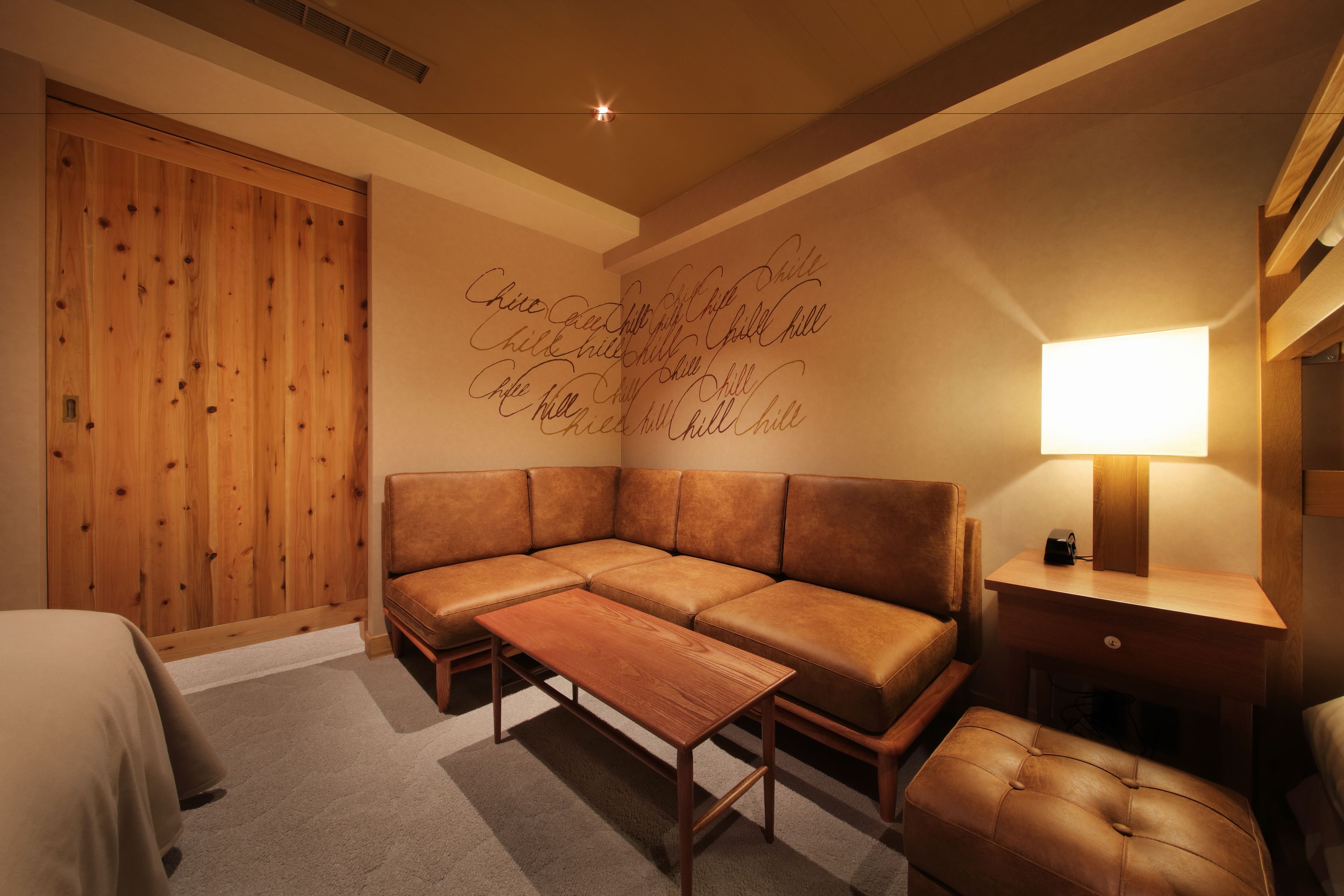 A modern room with a wooden wardrobe, a leather sofa, a wooden coffee table, and a bedside lamp.