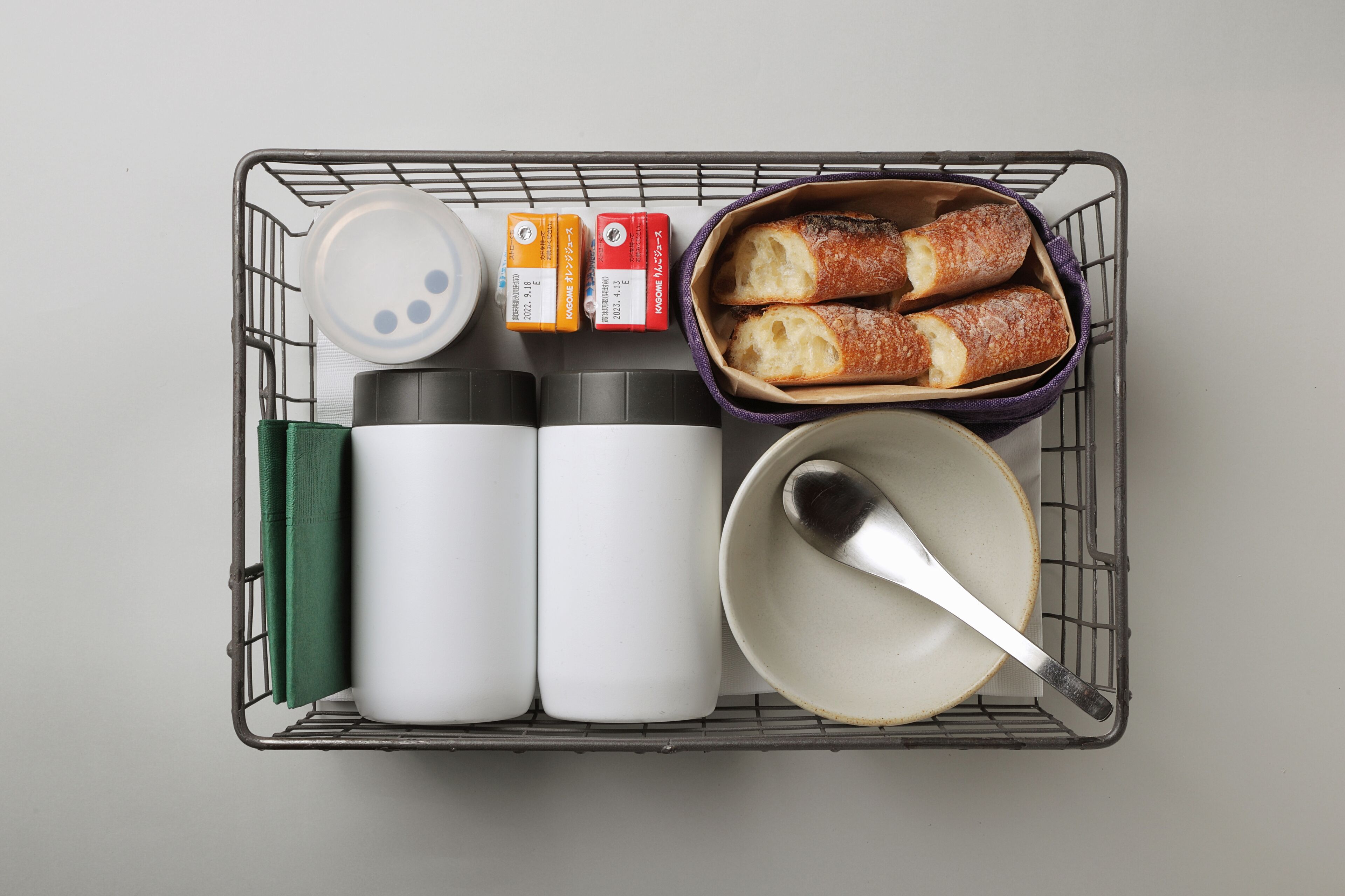 A shopping cart with a bread box, milk cartons, a green cloth, and a white plate with a spoon.