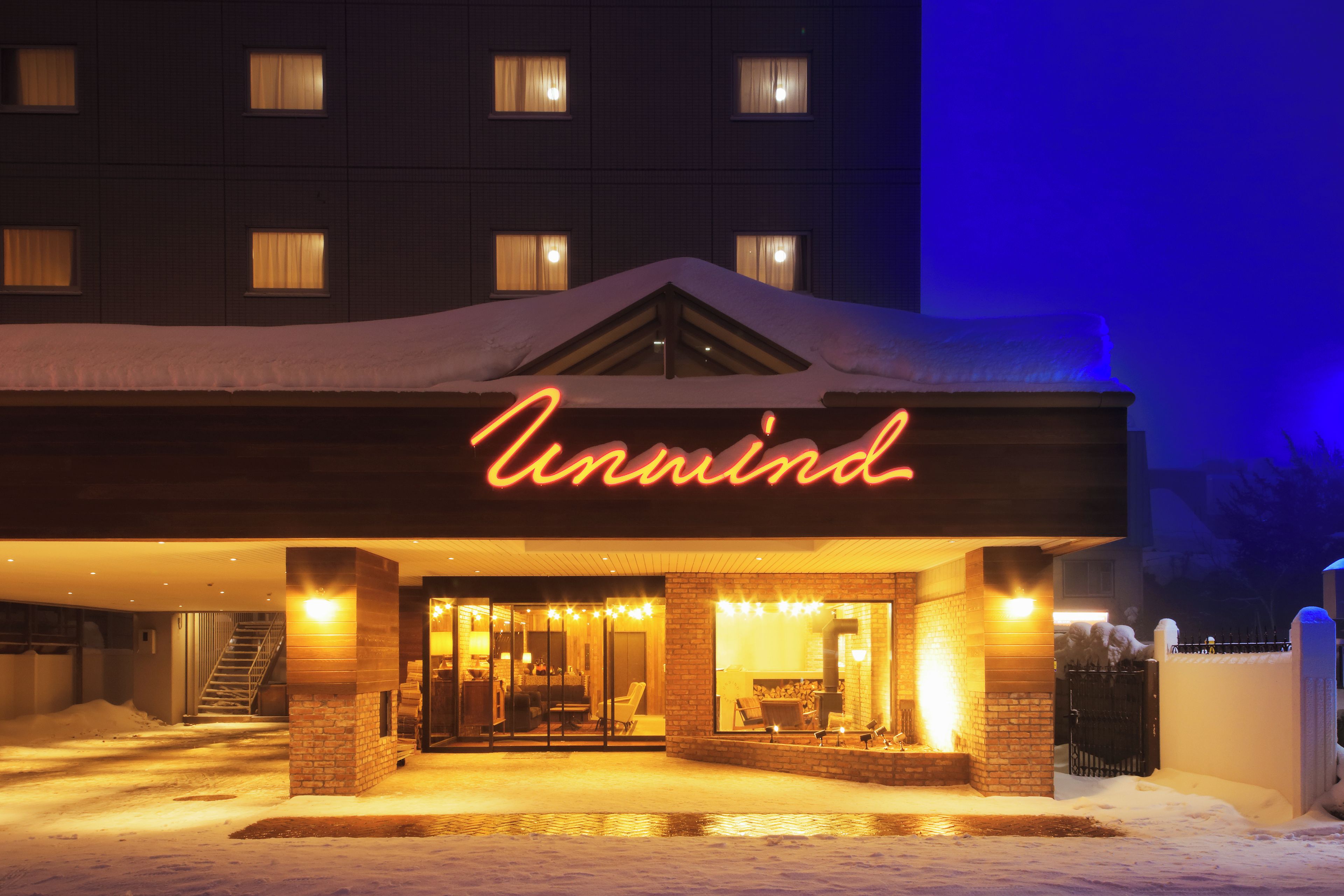 A hotel entrance with a neon sign, a covered outdoor seating area, and a snow-covered ground.