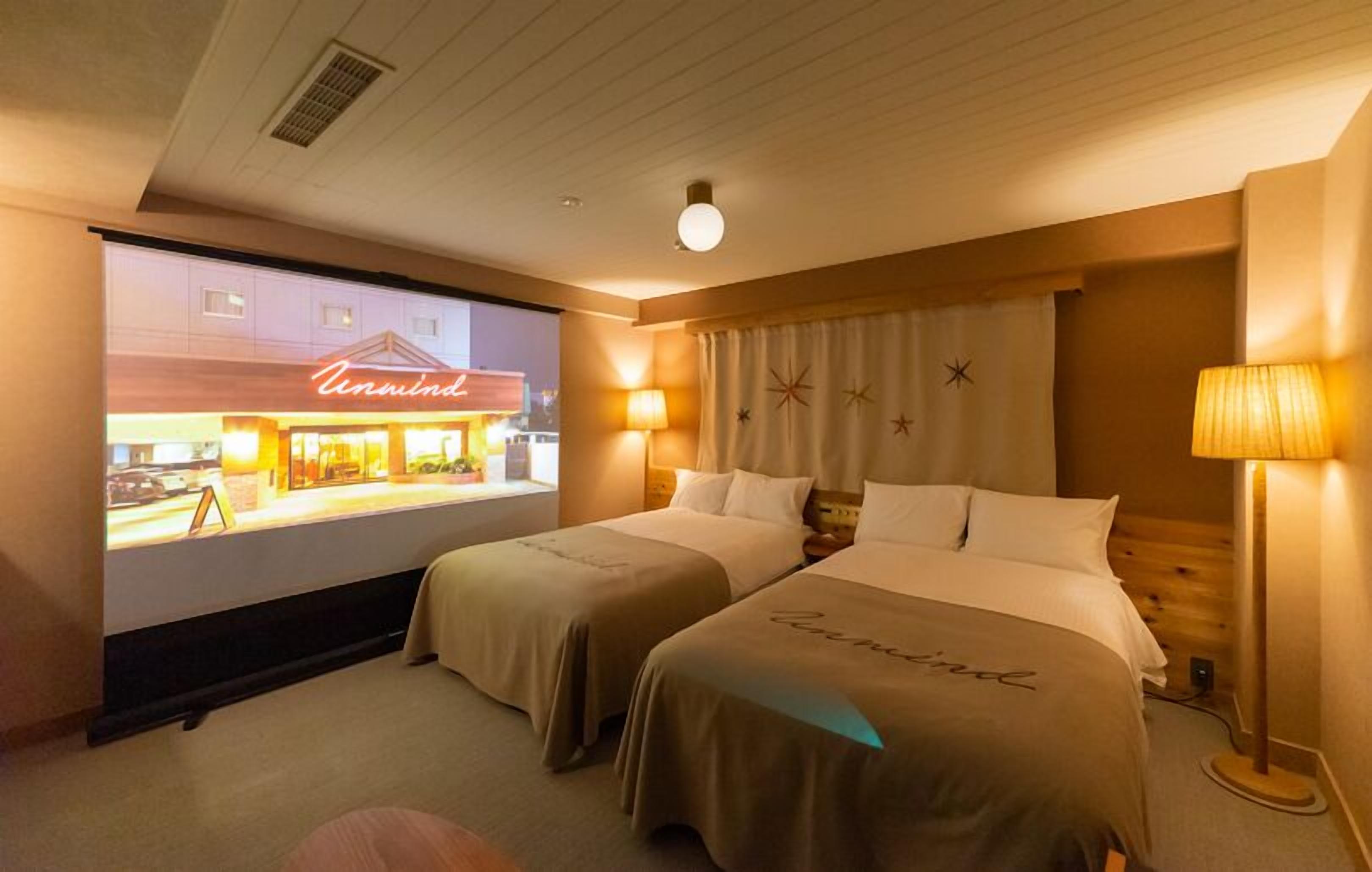 A hotel room with two beds, a projector screen displaying a restaurant, and a lamp.