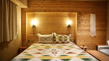 A wooden-paneled room with a bed, two wall-mounted lights, a macrame wall hanging, and a small round table.