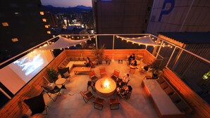 A rooftop terrace with a fire pit, seating, and a large screen. - Unwind Hotel & Bar Sapporo (Sapporo)