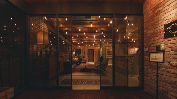 A warmly lit interior with a brick wall, a glass door entrance, and a seating area visible through the glass. - Unwind Hotel & Bar Sapporo (Sapporo)