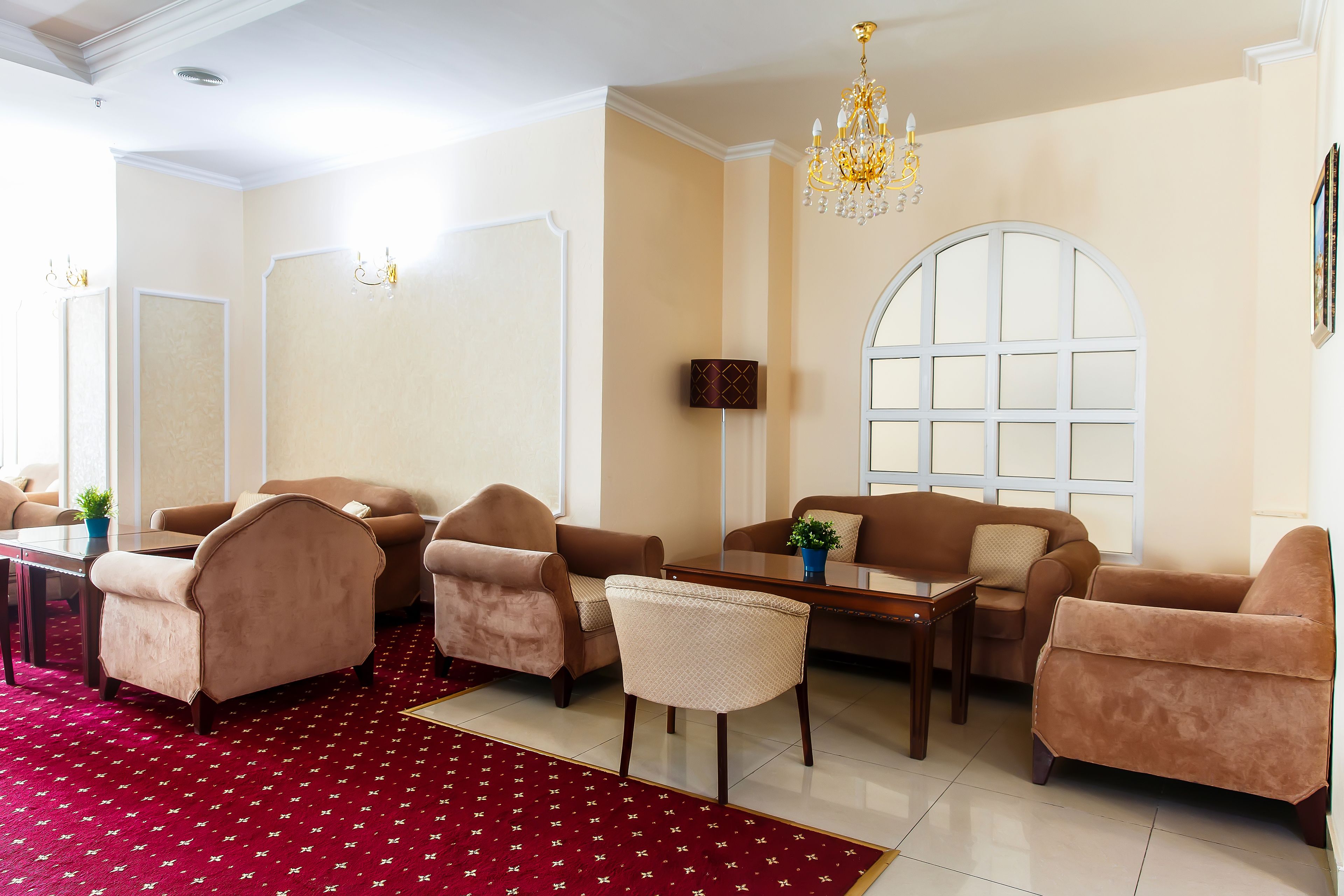 A spacious living room with beige walls, a red patterned carpet, and a large arched window.