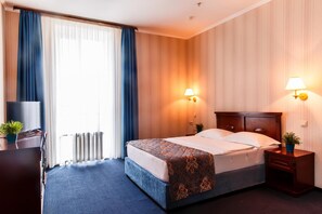 Una habitación de hotel con cama, dos lámparas de noche, televisor, escritorio y ventana con cortinas.