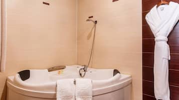 A bathroom with a freestanding bathtub, two towels, a robe hanging on the wall, and a showerhead.