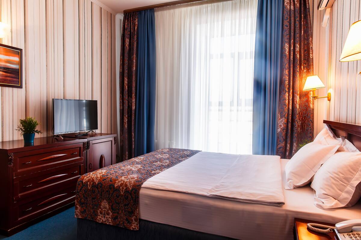Una habitación de hotel con cama, escritorio con televisor, teléfono y lámpara.