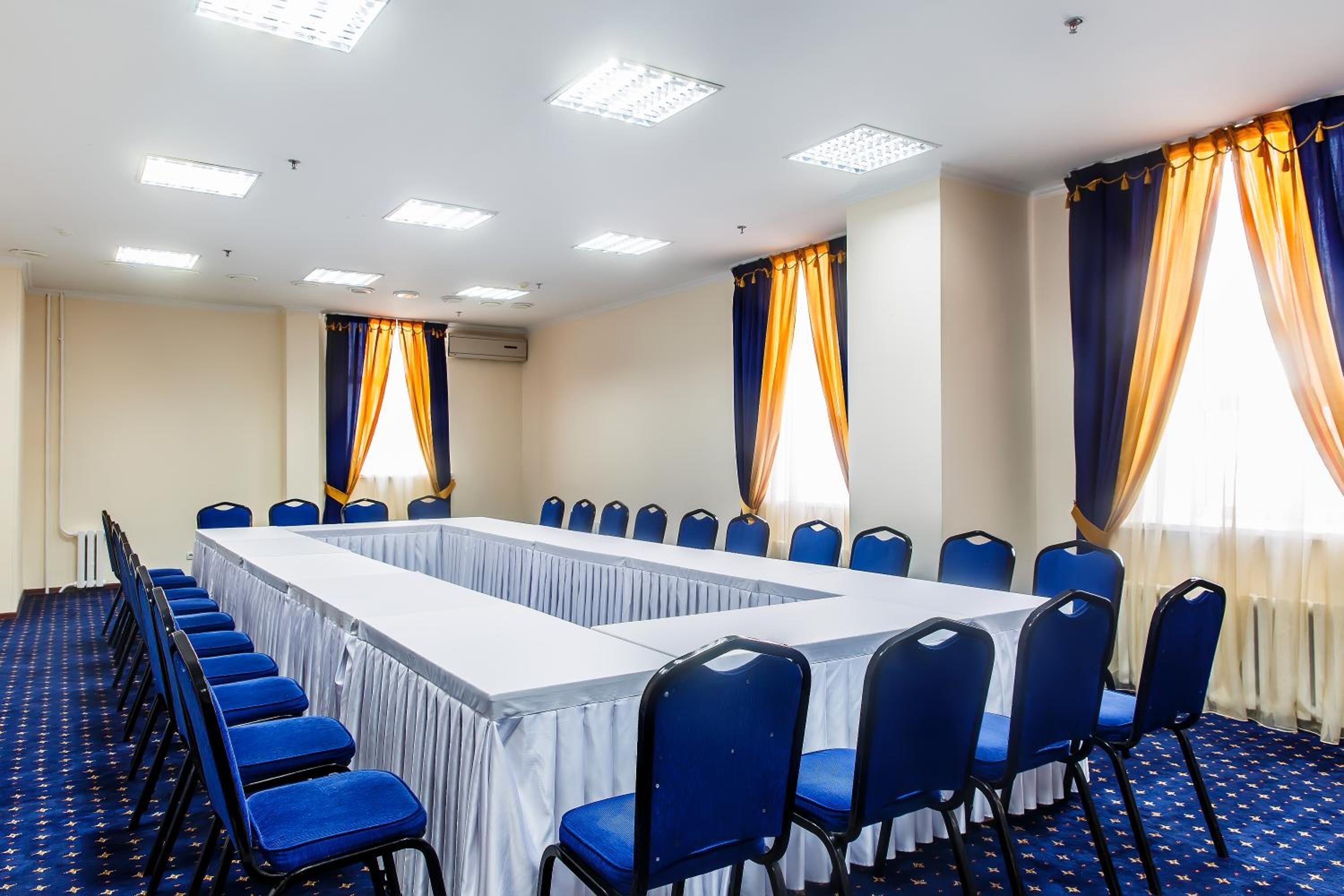 Ein Konferenzraum mit einem langen Tisch, blauen Stühlen und Vorhängen.