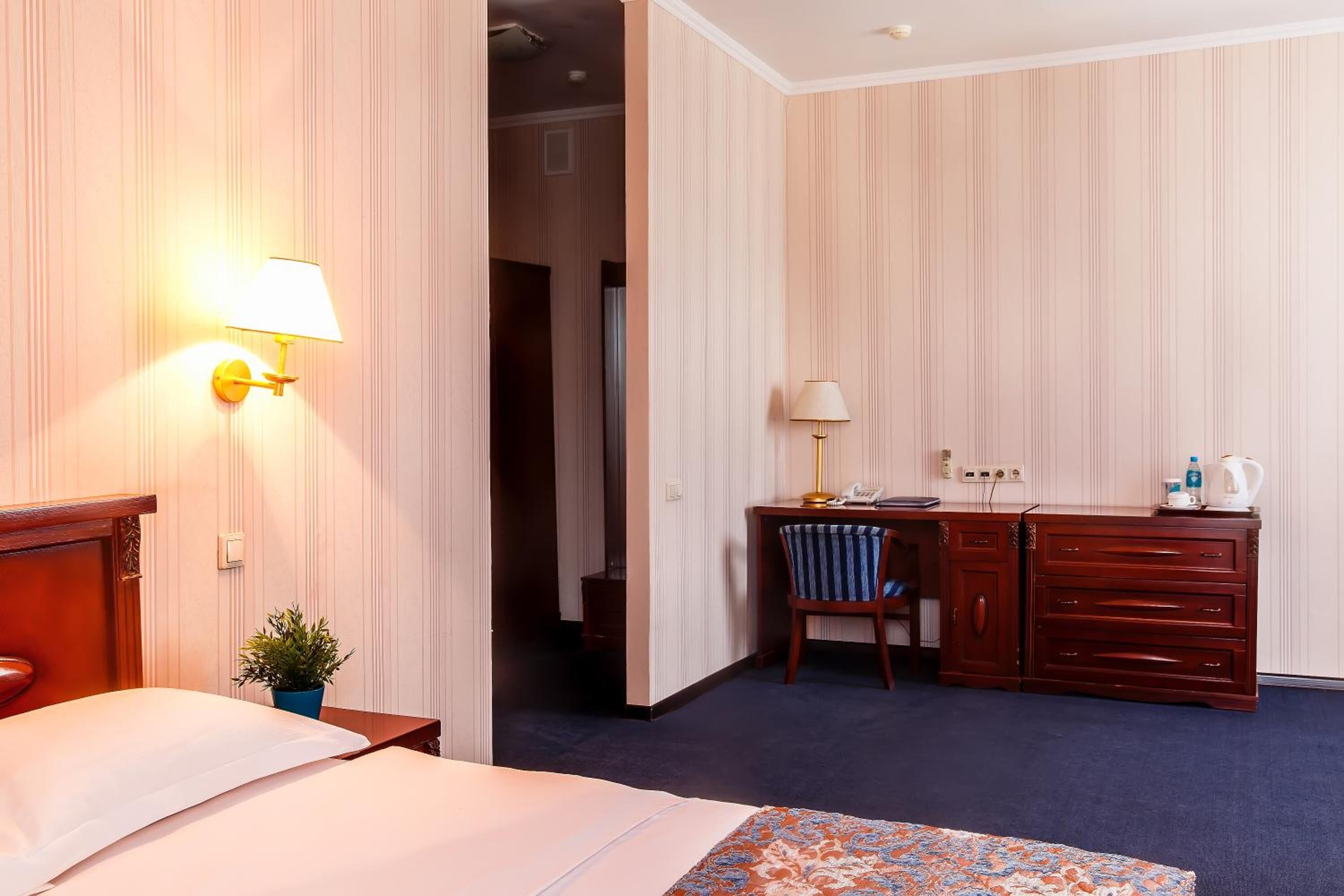 Una habitación de hotel con cama, escritorio y silla, cómoda y mesita de noche con lámpara.