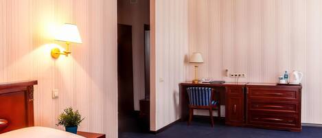 Una habitación de hotel con cama, escritorio y silla, cómoda y mesita de noche con lámpara.