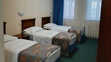 Une chambre d’hôtel avec trois lits, une moquette verte et une fenêtre avec des rideaux blancs.