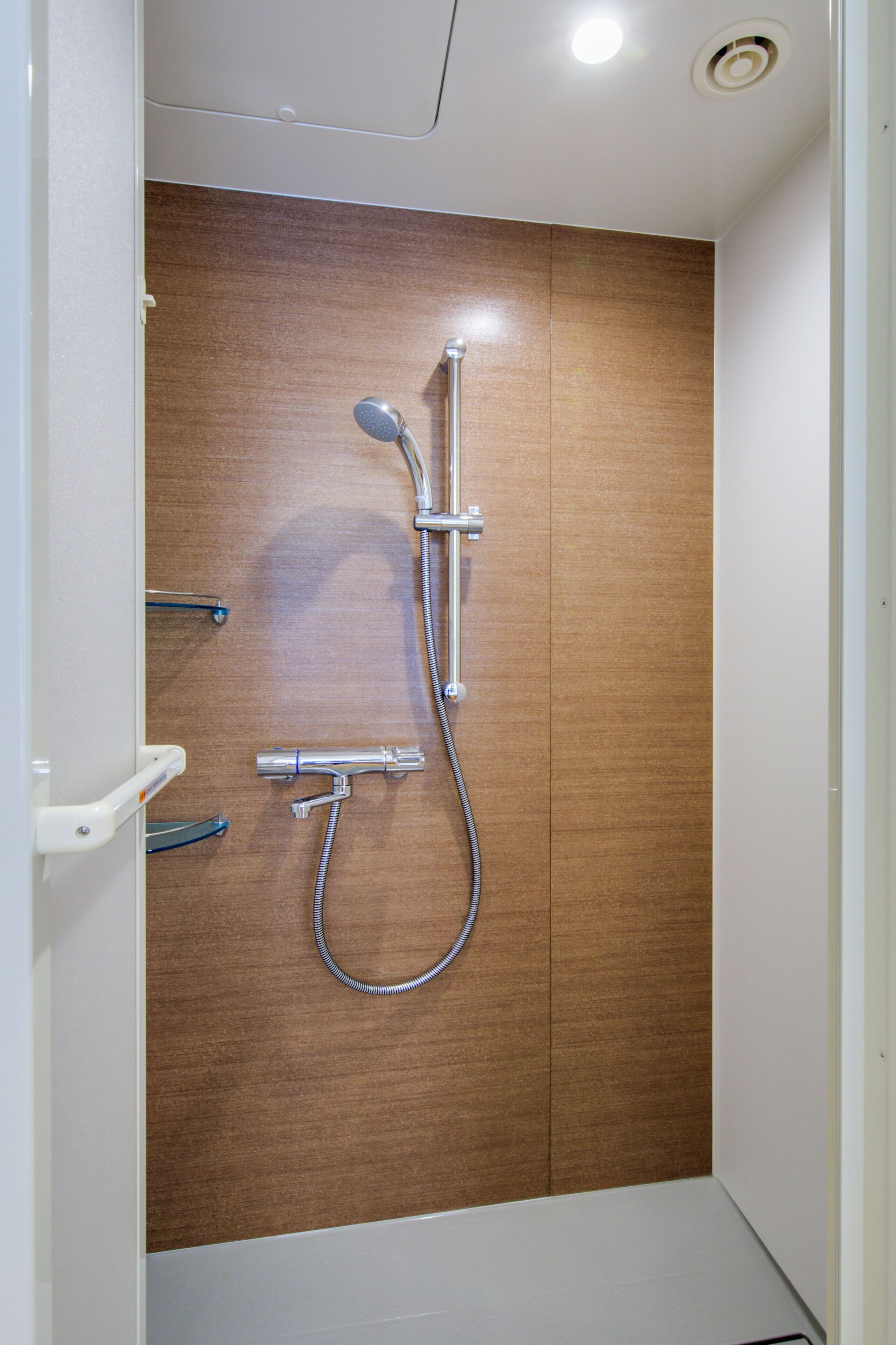 A shower with a wooden panel wall, a handheld showerhead, and a wall-mounted faucet.