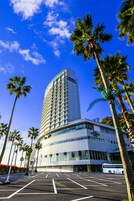 Un hotel dal design moderno, con una torre imponente e un parcheggio con palme.