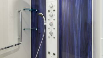 A walk-in shower with a glass door, a handheld showerhead, and a control panel with multiple knobs.