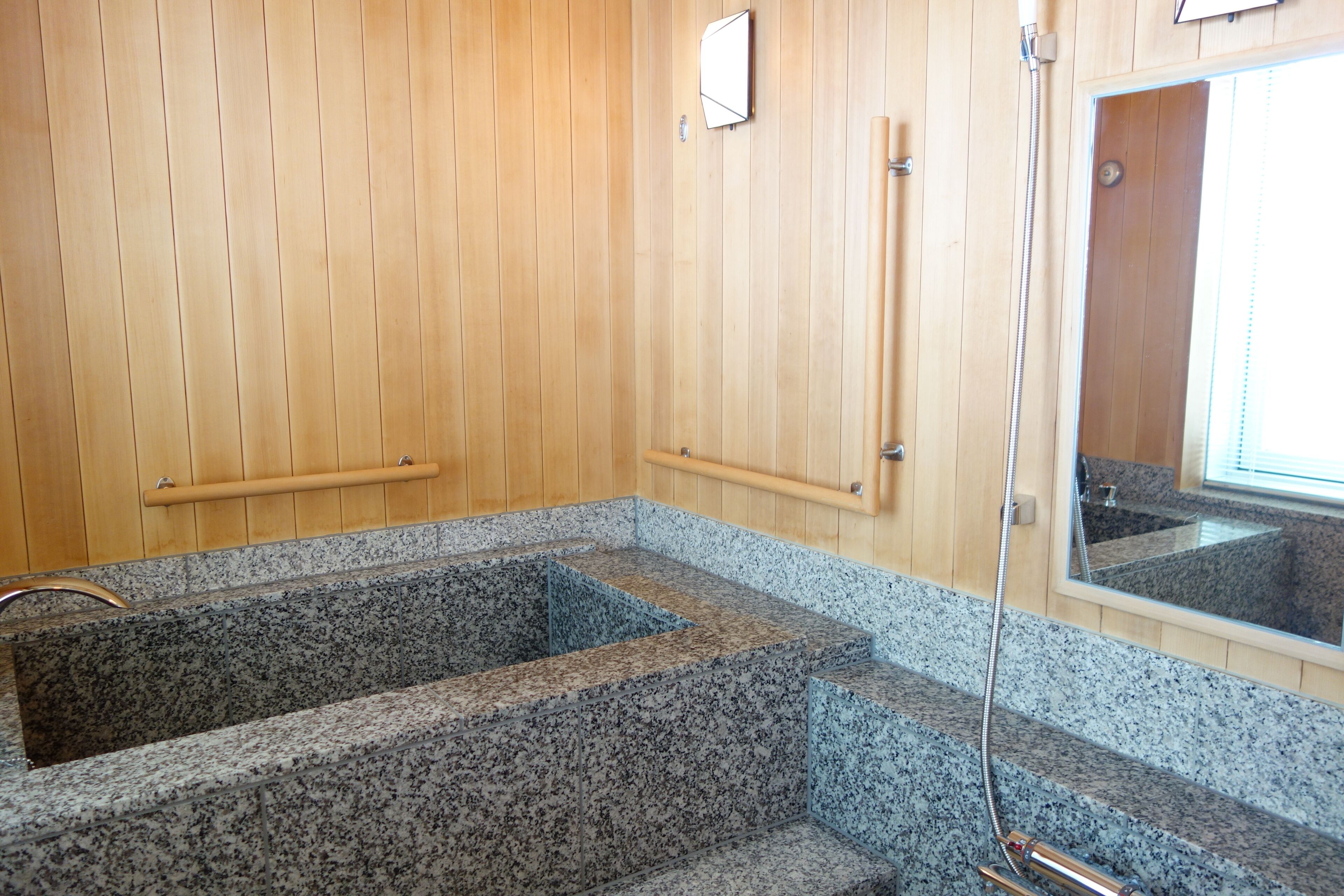 Un spa de madera con bañera de hidromasaje de granito, paredes de madera y un espejo que refleja el interior.