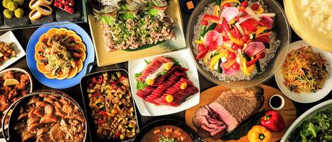 Forskellige retter, herunder sushi, pasta og en kødret, anrettet på et bord.