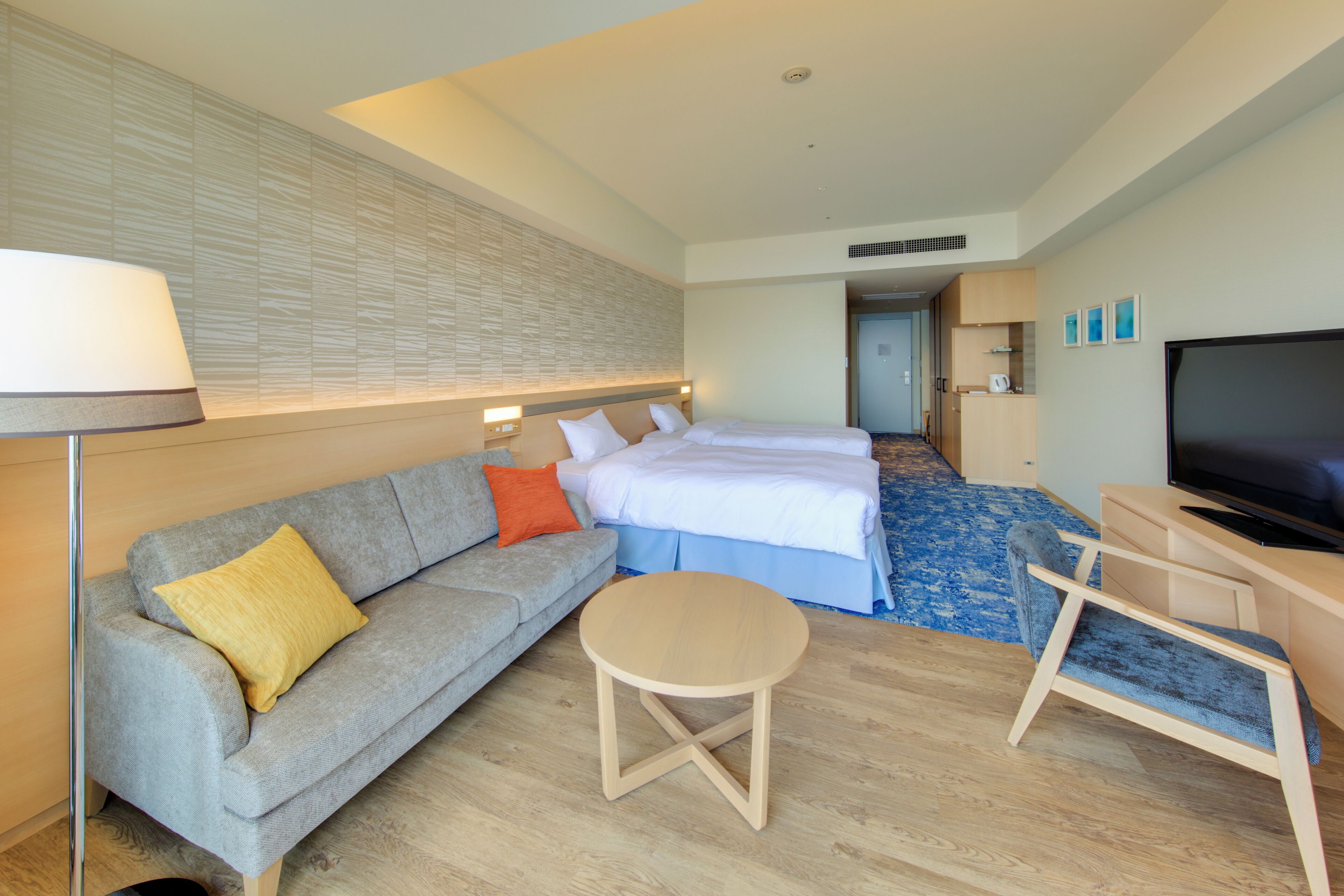A hotel room with a sofa, a bed, a TV, a small table, and a desk.