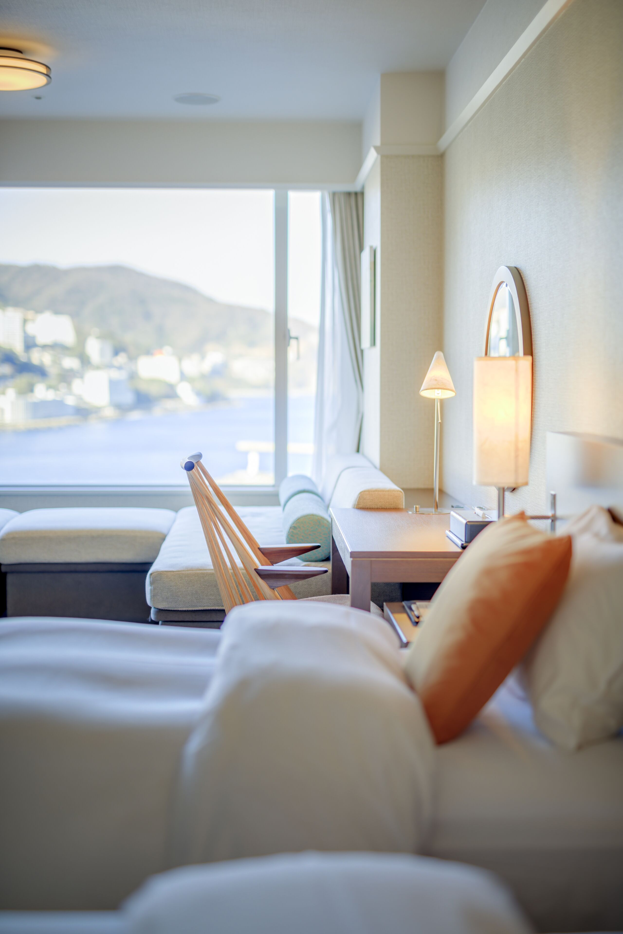 A hotel room with a bed, a bedside table, a lamp, and a view of the sea.