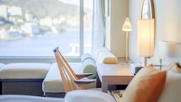 A hotel room with a bed, a bedside table, a lamp, and a view of the sea.