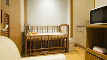 A baby crib with toys, a changing table, a microwave, and a cabinet in a room with wooden flooring and walls.