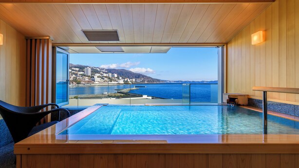 A modern indoor swimming pool with a view of a coastal city. - Atami Korakuen Hotel (Atami)