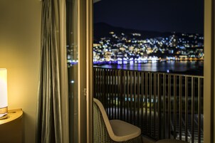 A balcony with a view of a cityscape at night, a lamp, and a chair.