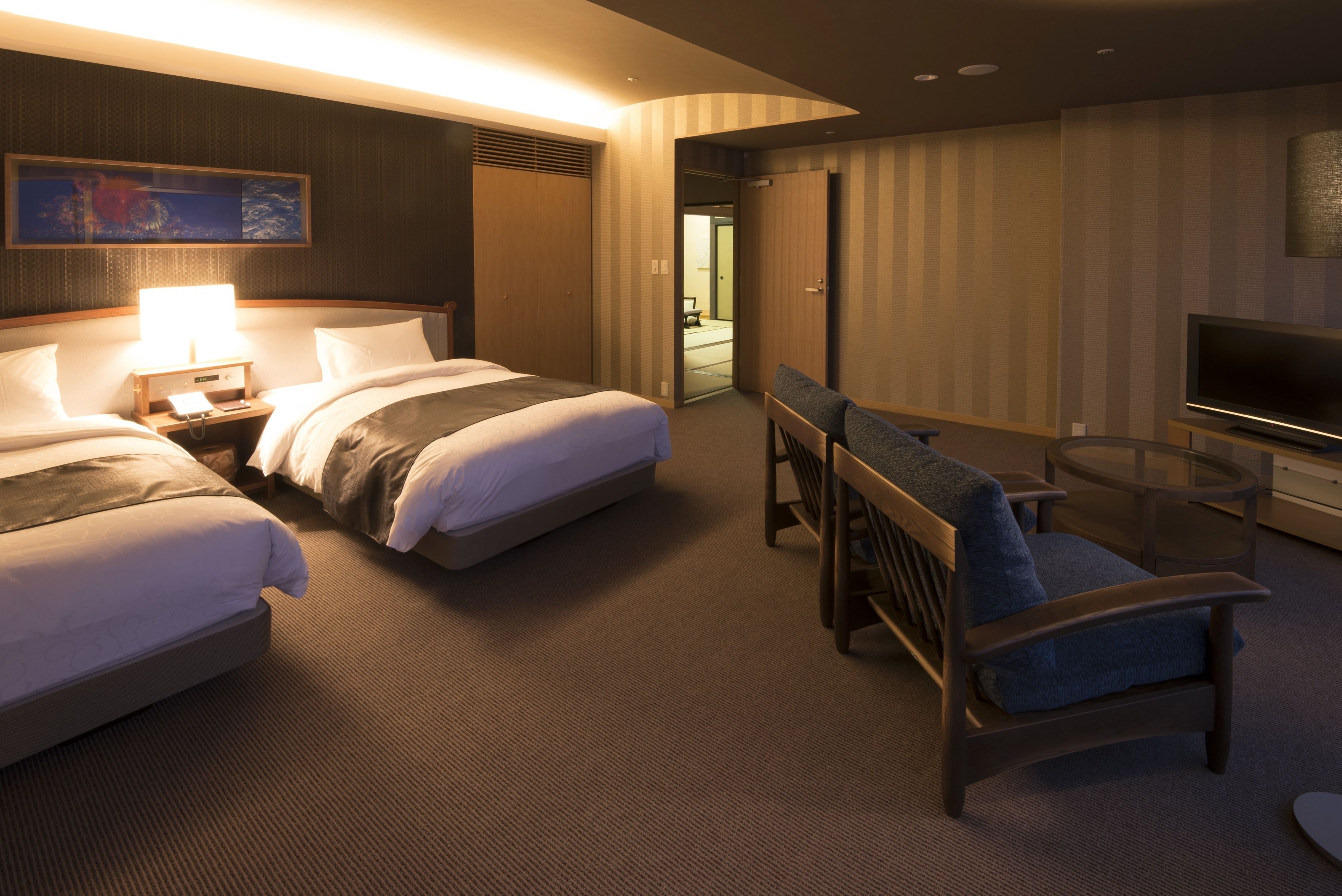 A hotel room with two beds, a desk, a chair, a television, and a painting on the wall.