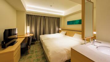 A hotel room with a bed, a desk with a computer, a TV, a large mirror, and a bathroom with a sink and toilet.
