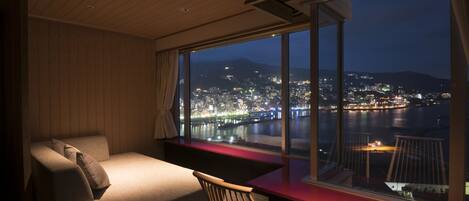 Un balcon avec un canapé et des fauteuils, donnant sur une vue panoramique de la ville la nuit.