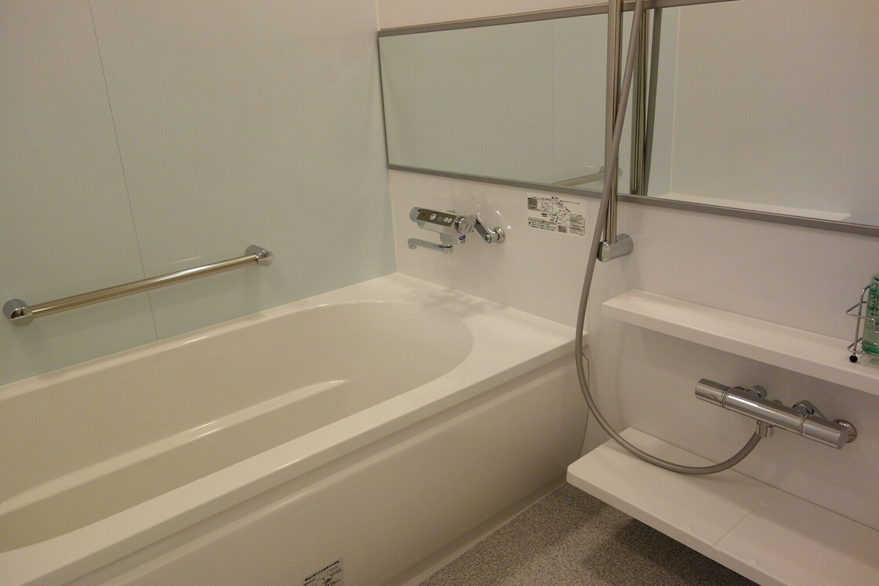 Un baño con una bañera blanca, un pasamanos, zona de ducha y un espejo.
