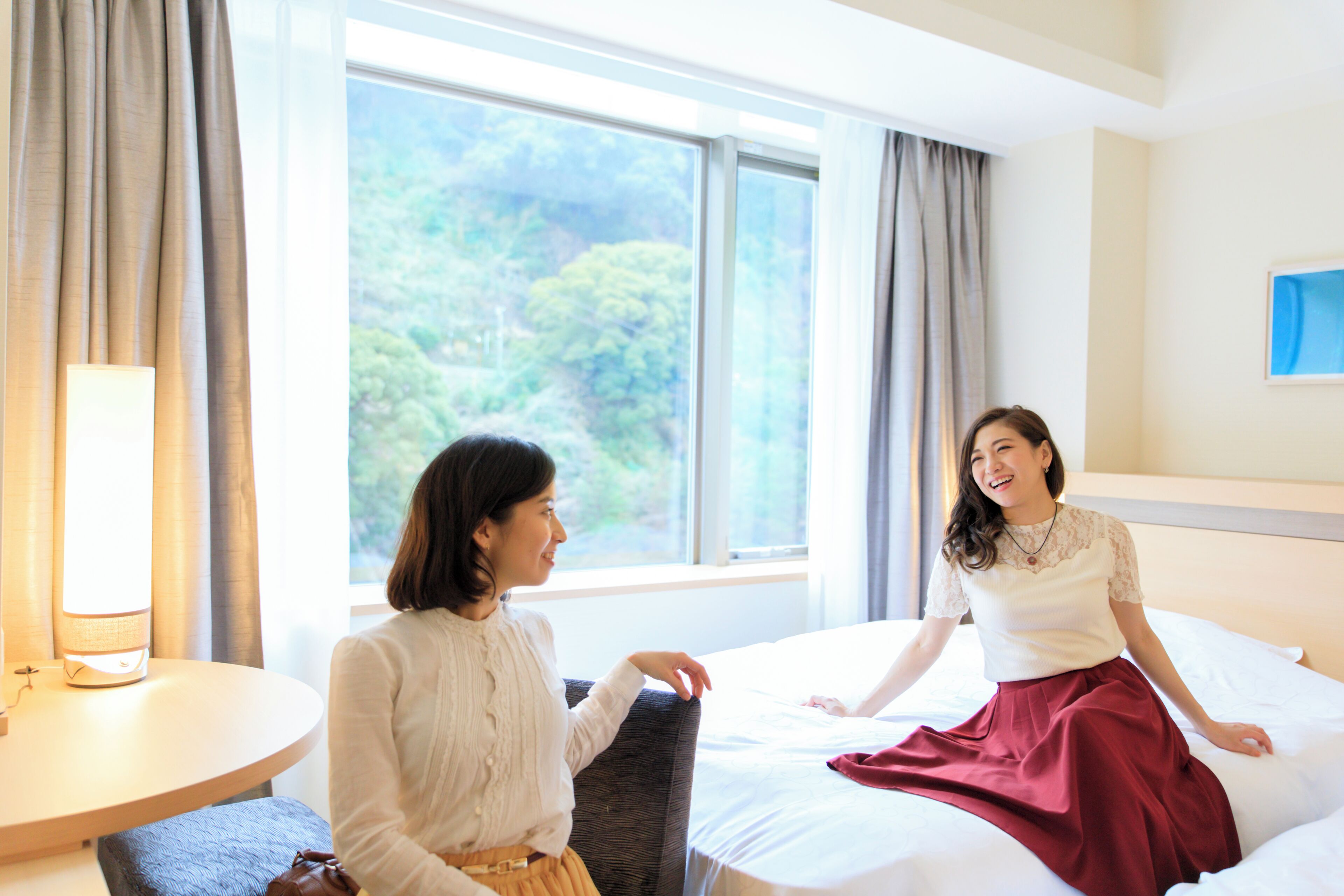 A hotel room with a bed, a round table, and a view of greenery outside.