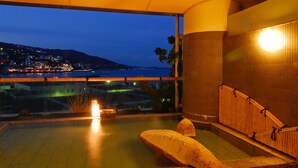 A spa area with a hot tub, a view of the cityscape at dusk, and a pool with a stone sculpture. - Atami Korakuen Hotel (Atami)