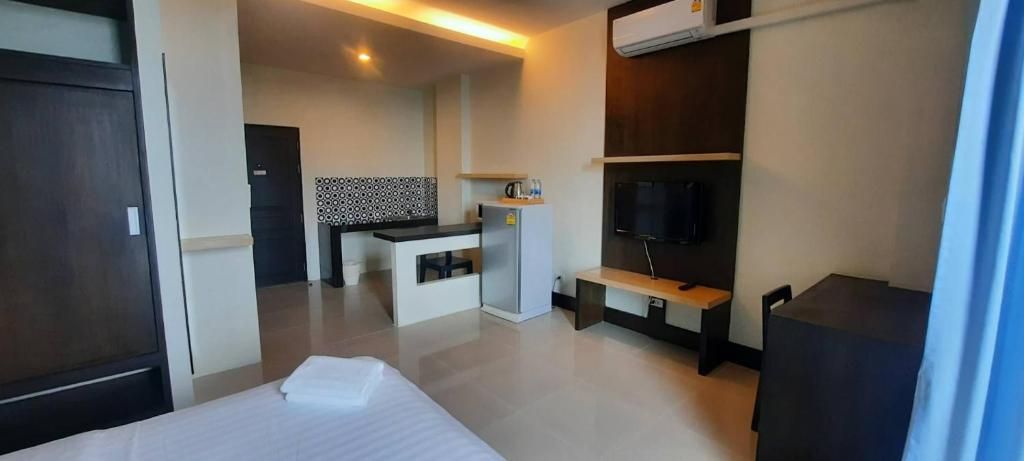 A hotel room with a bed, a small kitchenette, a TV, and a desk.