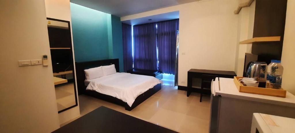 Habitación de hotel con cama, escritorio, silla, mesita y ventana con cortinas.