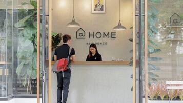 Welcome to HOME RESIDENCE, where guests are greeted by a modern reception area featuring a central desk and lush greenery.