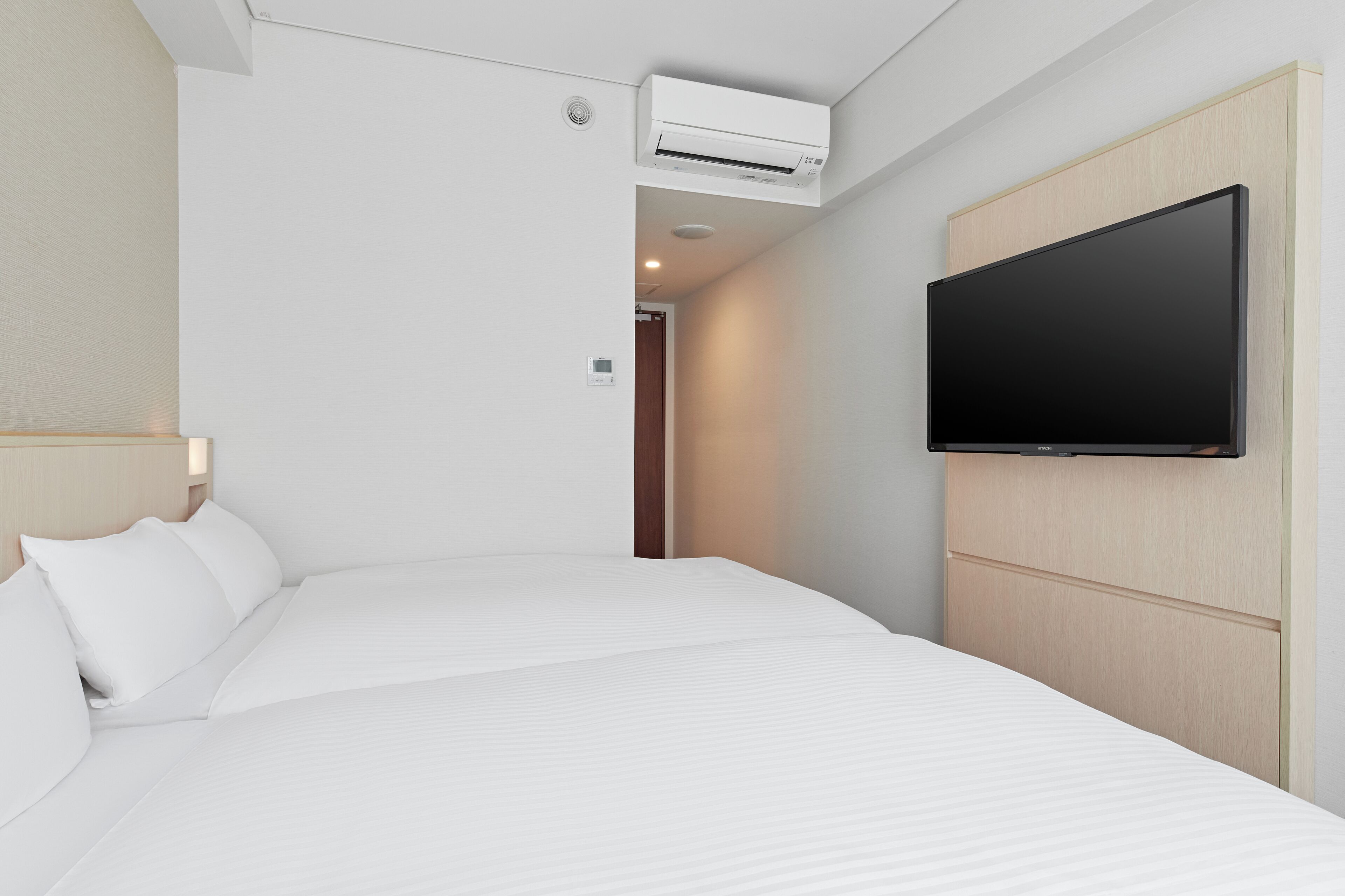 Ein Hotelzimmer mit einem großen Bett, einem an der Wand befestigten Fernseher und einer Klimaanlage.