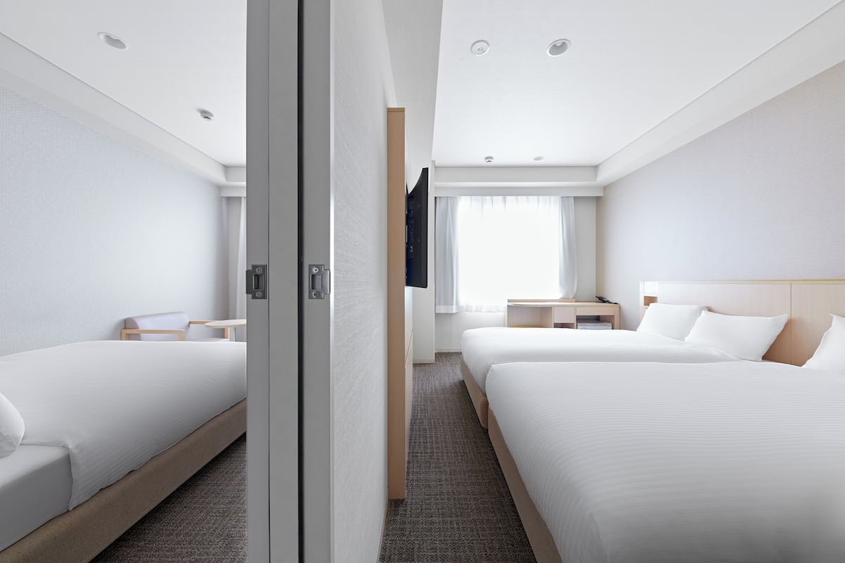 Ein Hotelzimmer mit zwei Betten, einem Flachbildfernseher, einem Nachttisch und einem Fenster mit Vorhängen.