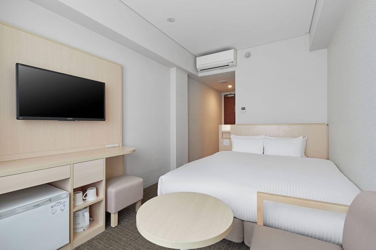 Ein Hotelzimmer mit Bett, Fernseher, Schreibtisch, Stuhl, einem kleinen Tisch und einer Klimaanlage.