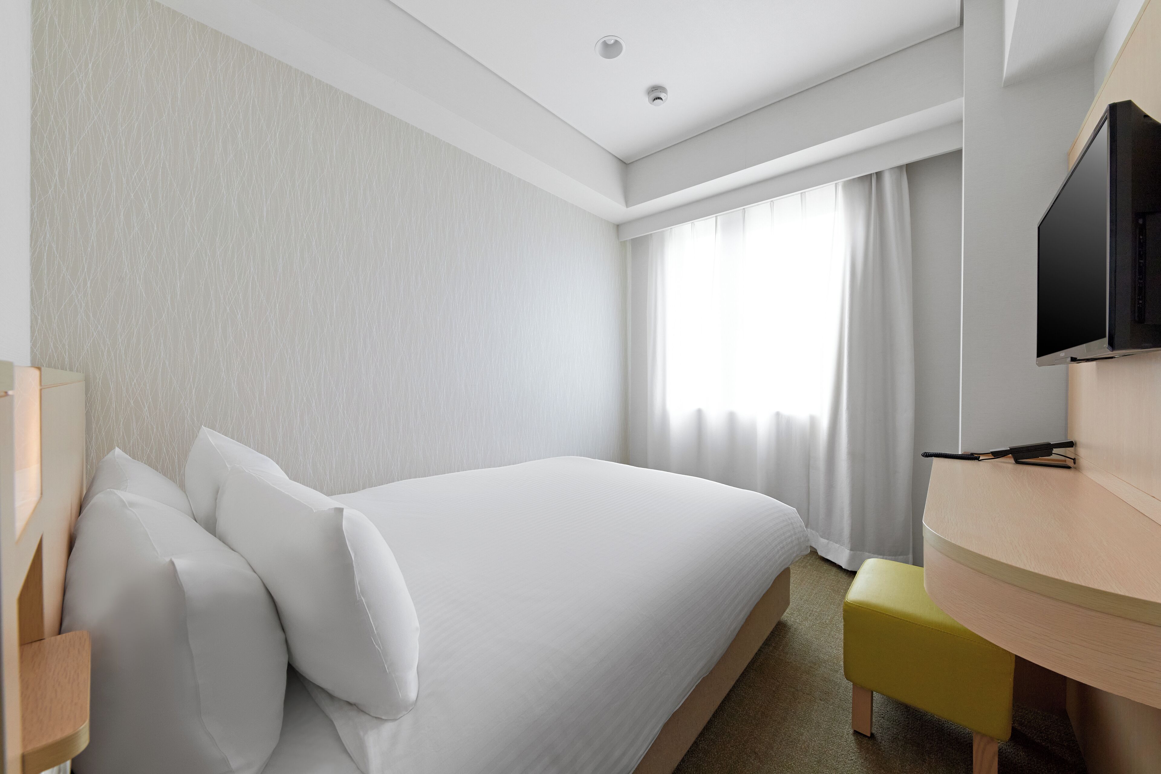 A hotel room with a bed, a desk, a chair, a television, and a window with curtains.