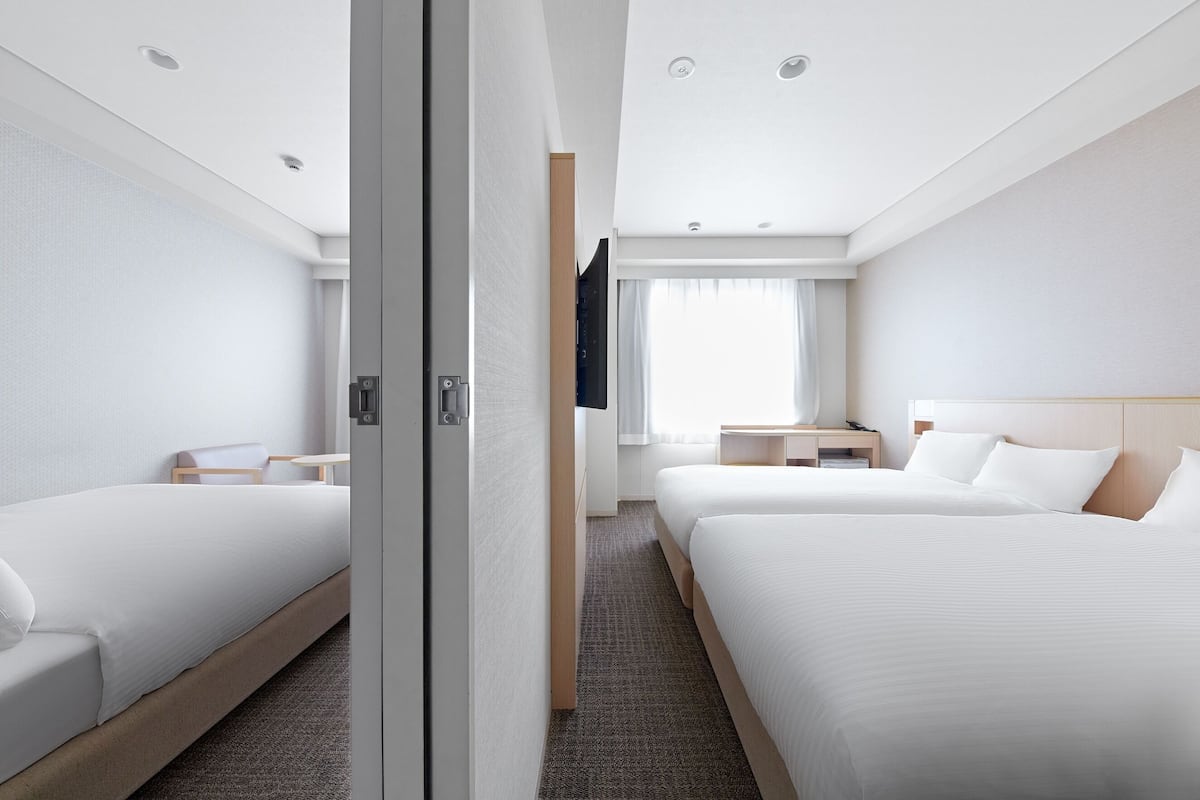Ein Hotelzimmer mit zwei Betten, einem Schrank, einem Schreibtisch und einem Fenster mit Vorhängen.