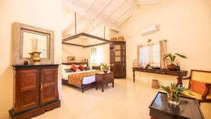 A spacious room with a large bed, a wooden cabinet, a small table, and a chair. - The Sun House (Galle)