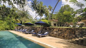 A poolside area with lounge chairs and umbrellas, surrounded by stone walls and palm trees. - The Dutch House (Galle)