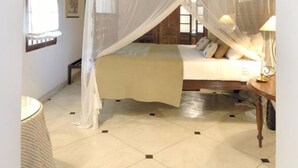 A bedroom with a canopy bed, a small bedside table, a lamp, and a window with curtains. - The Dutch House (Galle)