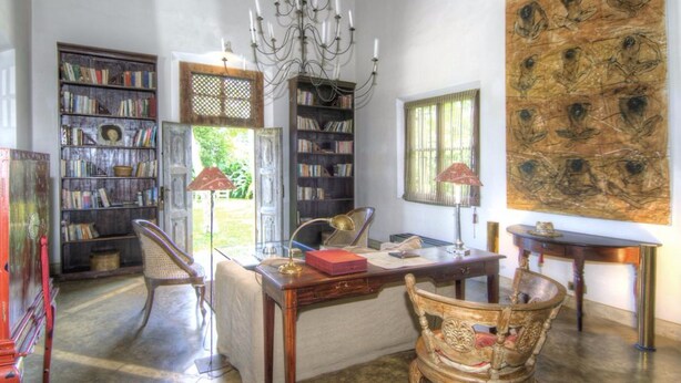 A library with bookshelves, a chandelier, and a large painting. - The Dutch House (Galle)
