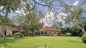 A well-maintained lawn with a dining area featuring wicker furniture and a table with a bottle. - The Dutch House (Galle)