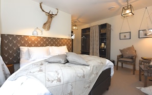A bedroom with a bed, a headboard with a deer antler, a wardrobe, a chair, and a hanging light fixture.