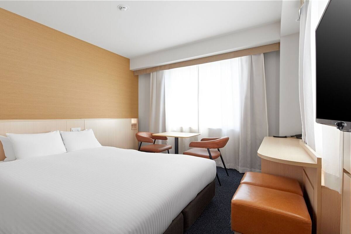 A hotel room with a large bed, a desk, a chair, and a TV.